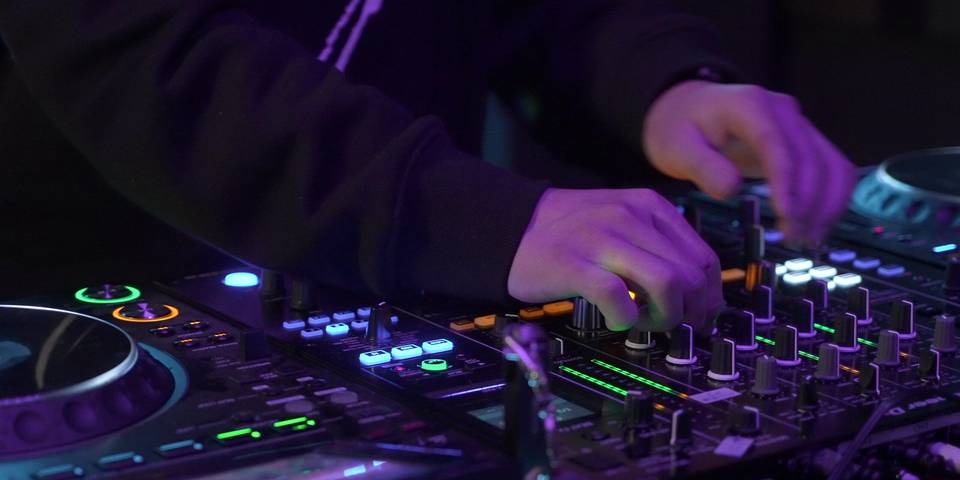 Loş ışıkta DJ mikserinin düğmelerini çeviren eller